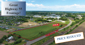 An aerial shot of a piece of land and other buildings. The main piece of land is outlined in red and marked "sold." On the top left is a square graphic with text that says, "Great Highway 55 Frontage." On the bottom right is a square graphic with text that reads, "PRICE REDUCED."