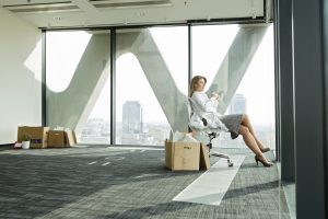Businesswoman on empty office floor with cardboard box looking out of window